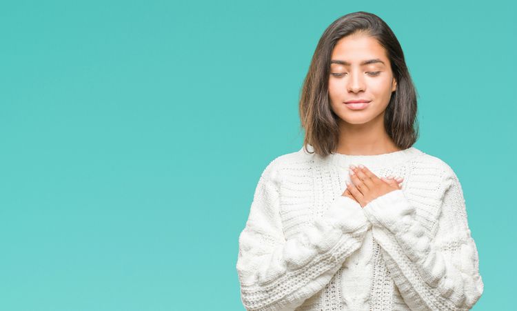 woman in white sweater holding hands over heart gratitude concept